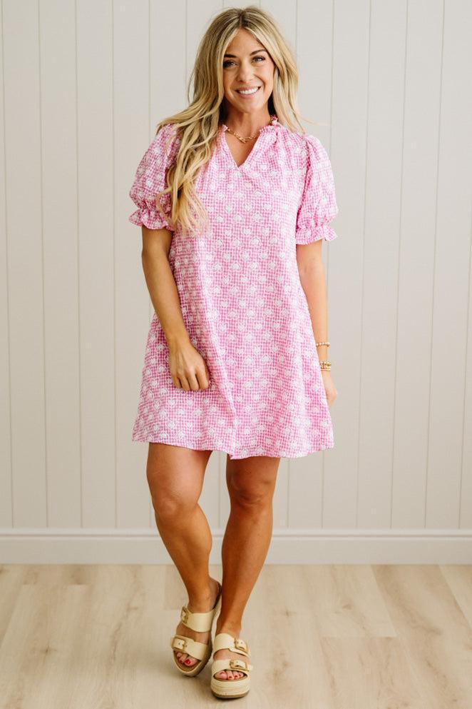 Woman wearing a pink checkered dress against a white wall.
