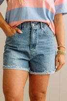 Person wearing a striped shirt and denim shorts against a neutral background