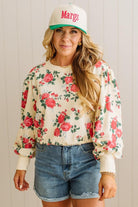 Woman wearing a floral sweatshirt, denim shorts, and a cap with 'Margs' text.