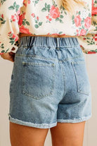 Person wearing light blue denim shorts with a floral top in the background