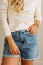 Person wearing a striped sweater and denim shorts with a neutral background