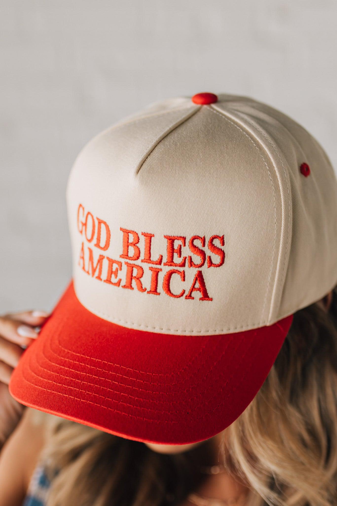 Blonde woman wearing a two tone cream and red trucker hat with GOD BLESS AMERICA embroidered at the front.