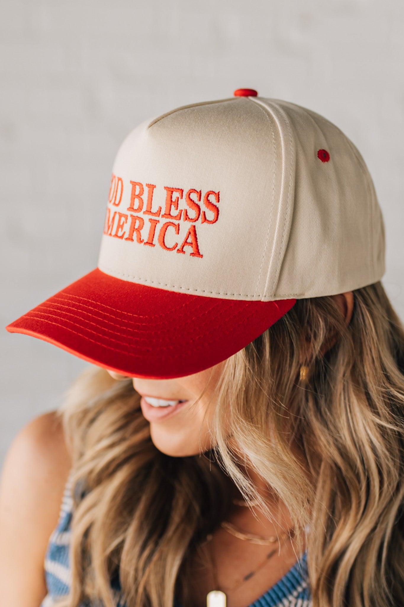 Blonde woman wearing a two tone cream and red trucker hat with GOD BLESS AMERICA embroidered at the front.