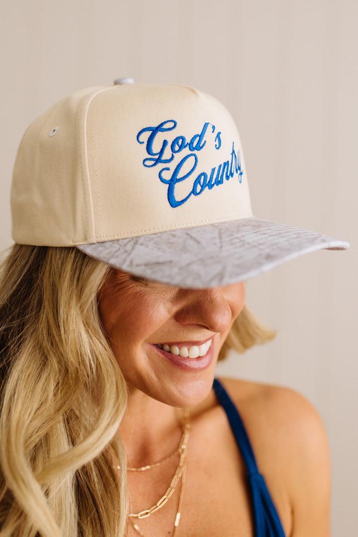 Woman wearing a beige cap with 'God's Country' text on a plain background