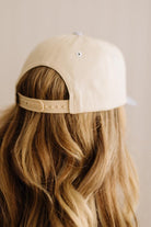 Beige cap worn by a person with wavy hair on a neutral background