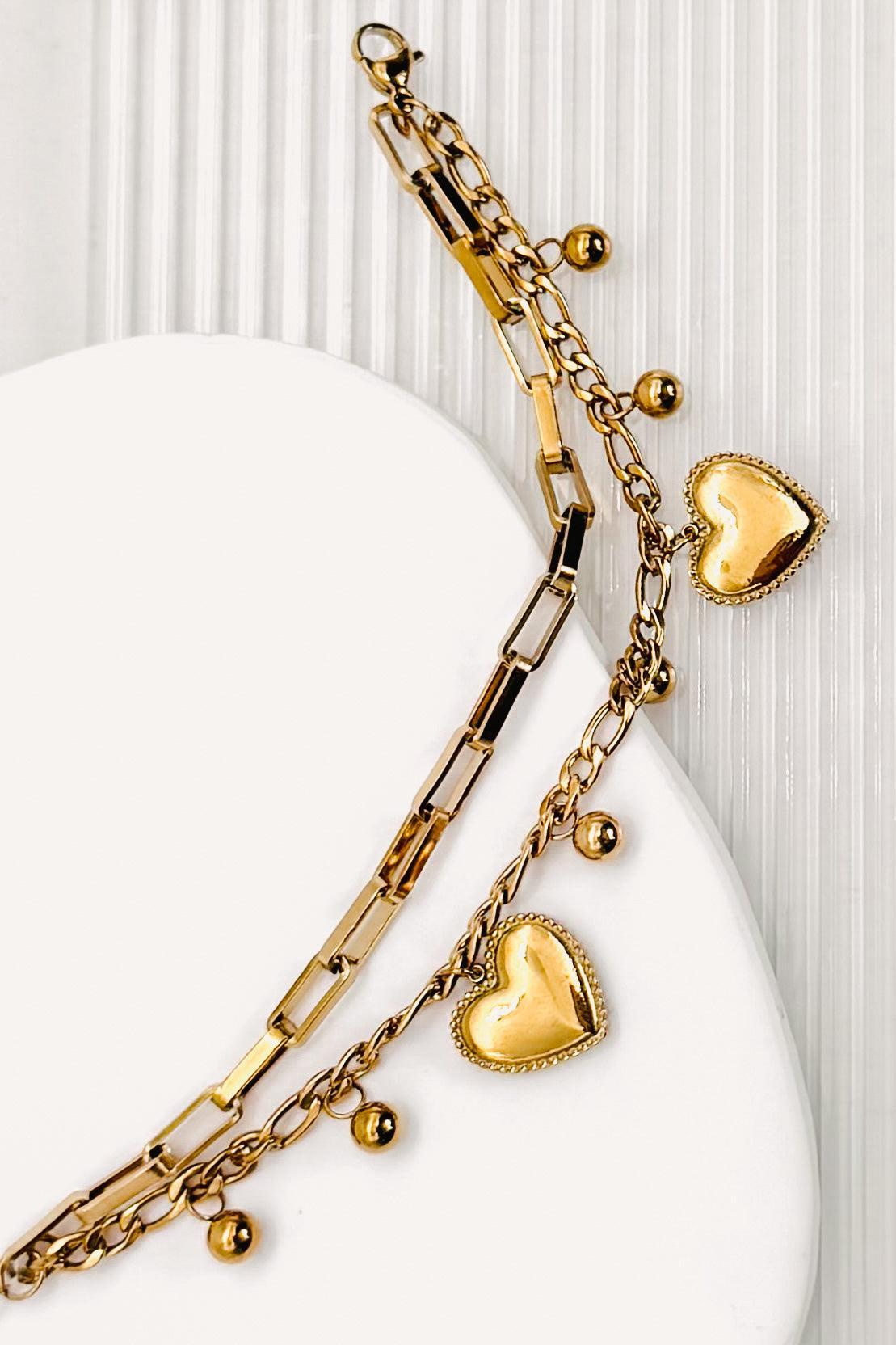 Close up of a 18k Gold Plated Waterproof Stainless Steel Bracelet with Heart and dot charms on a white stone surface.