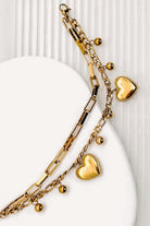 Close up of a 18k Gold Plated Waterproof Stainless Steel Bracelet with Heart and dot charms on a white stone surface.