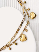 Close up of a 18k Gold Plated Waterproof Stainless Steel Bracelet with Heart and dot charms on a white stone surface.