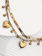 Close up of a 18k Gold Plated Waterproof Stainless Steel Bracelet with Heart and dot charms on a white stone surface.