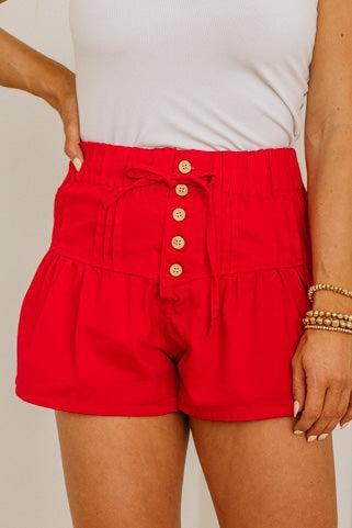 Red shorts with gold buttons worn by a person on a plain background
