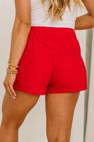 Person wearing red shorts and a white top against a neutral background