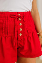 Red shorts with button details worn by a person, against a neutral background