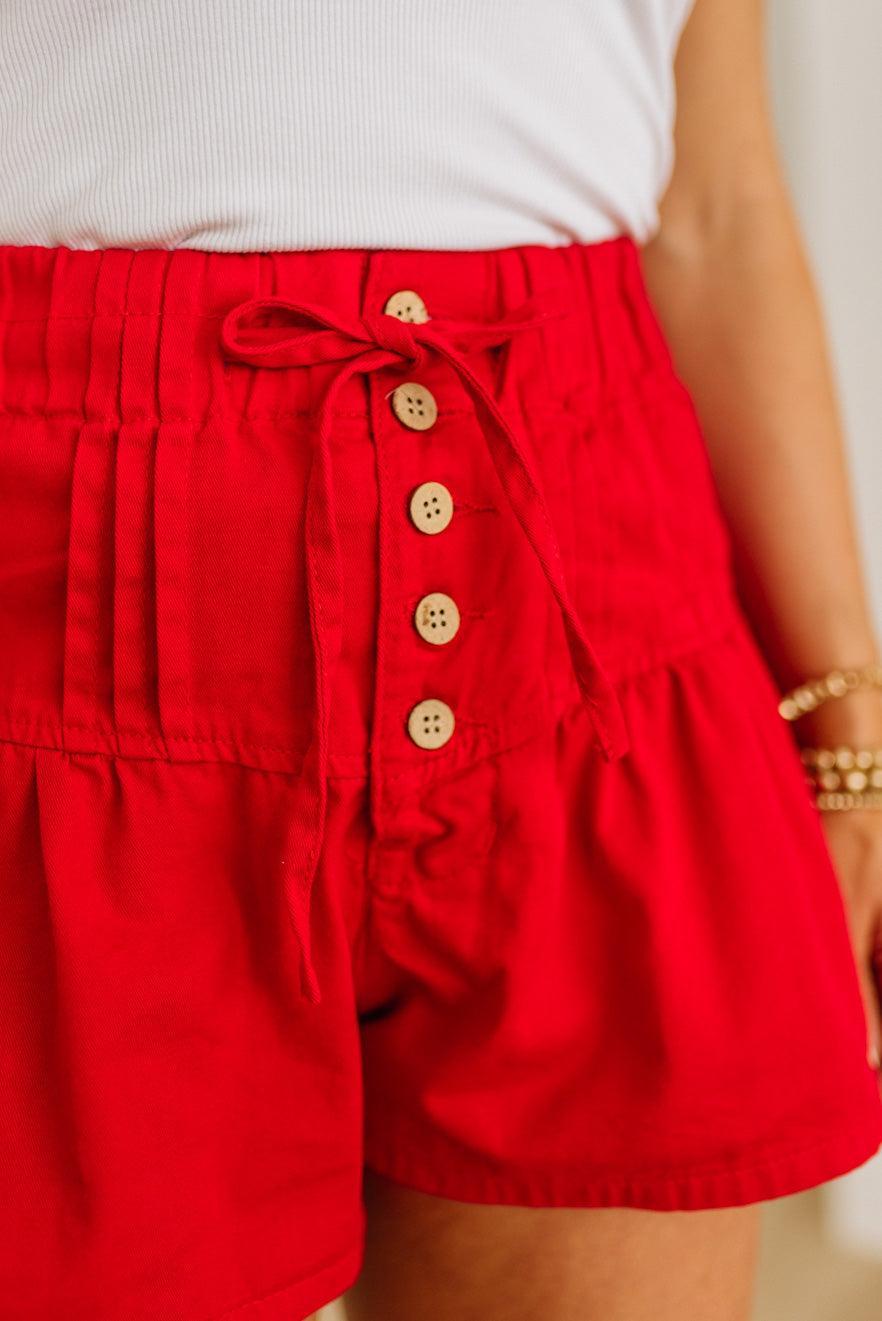 Red shorts with button details worn by a person, against a neutral background