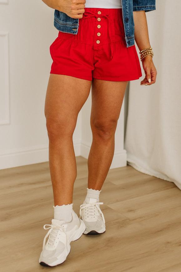 Person wearing red shorts, white sneakers, and a denim jacket on a wooden floor.