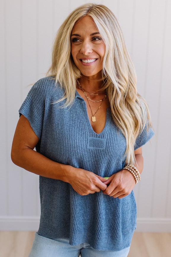 Blonde woman wearing a short sleeve v-neck ribbed texture sweater with center patch accent in blue.