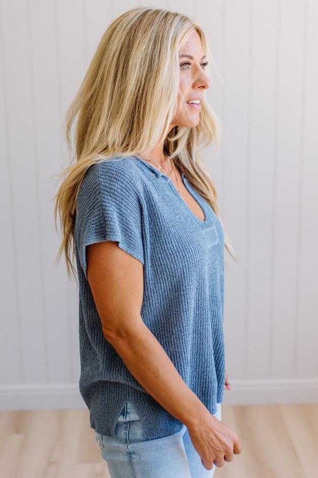 Blonde woman wearing a short sleeve v-neck ribbed texture sweater with center patch accent in blue.