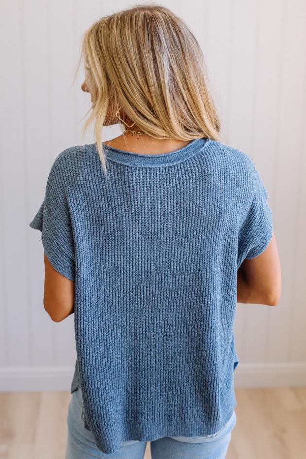 Blonde woman wearing a short sleeve v-neck ribbed texture sweater with center patch accent in blue.
