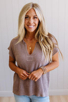 Blonde woman wearing a short sleeve v-neck ribbed texture sweater with center patch accent in mocha.