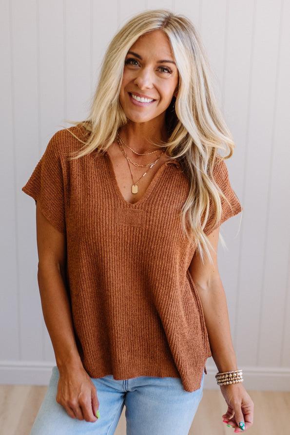 Blonde woman wearing a short sleeve v-neck ribbed texture sweater with center patch accent in rust.