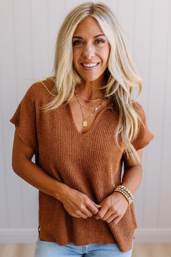 Blonde woman wearing a short sleeve v-neck ribbed texture sweater with center patch accent in rust.