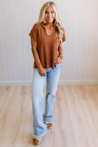 Blonde woman wearing a short sleeve v-neck ribbed texture sweater with center patch accent in rust.