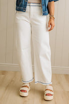 Person wearing white pants with blue trim, denim jacket, and sandals on a wooden floor.