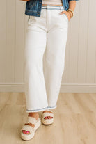 Person wearing white jeans with blue trim, a denim jacket, and sandals indoors.