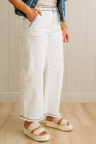 Person wearing white pants with blue trim, denim jacket, and sandals indoors.