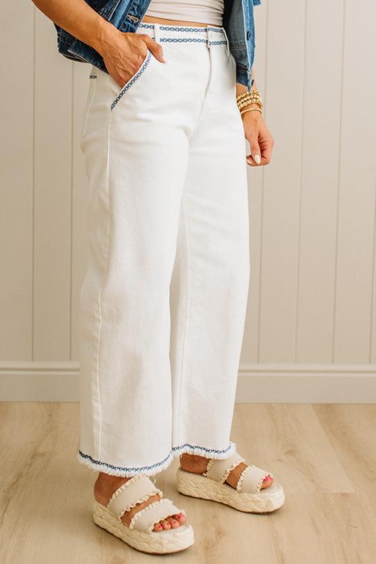 Person wearing white pants with blue trim, denim jacket, and sandals indoors.