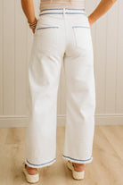 Person wearing white pants with blue trim standing against a light-colored wall.