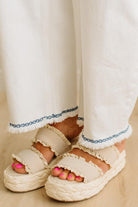 White sandals worn with white pants on a neutral background