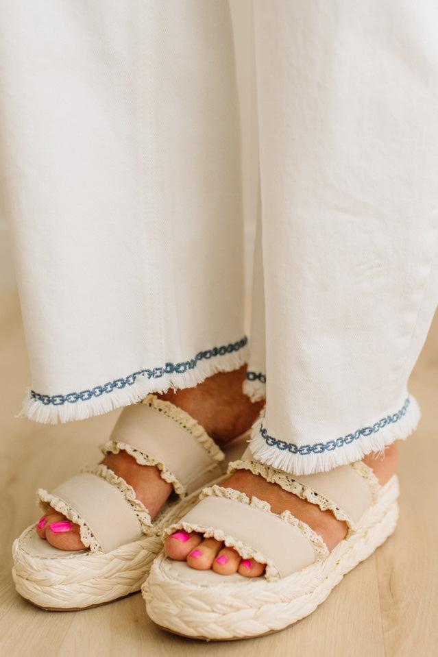 White sandals worn with white pants on a neutral background