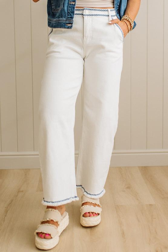 Person wearing white jeans with blue trim, a striped shirt, and sandals indoors.