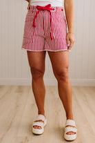 Woman wearing red and white striped shorts with red braided belt through grommets on waist. 