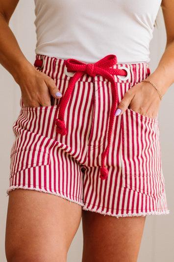 Woman wearing red and white striped shorts with red braided belt through grommets on waist. 
