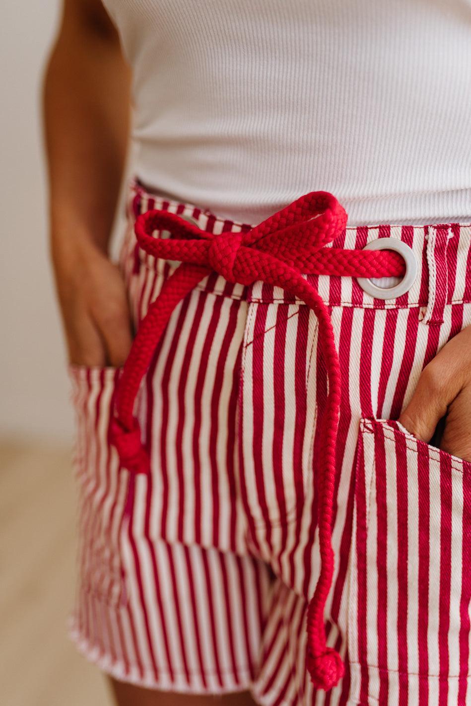 Woman wearing red and white striped shorts with red braided belt through grommets on waist. 