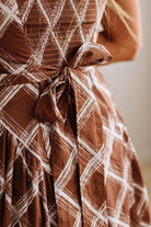 Close-up of a brown and white plaid dress with a matching fabric tie belt at the waist, worn by a model.