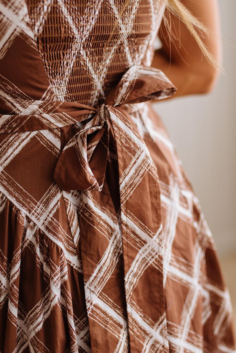 Close-up of a brown and white plaid dress with a matching fabric tie belt at the waist, worn by a model.