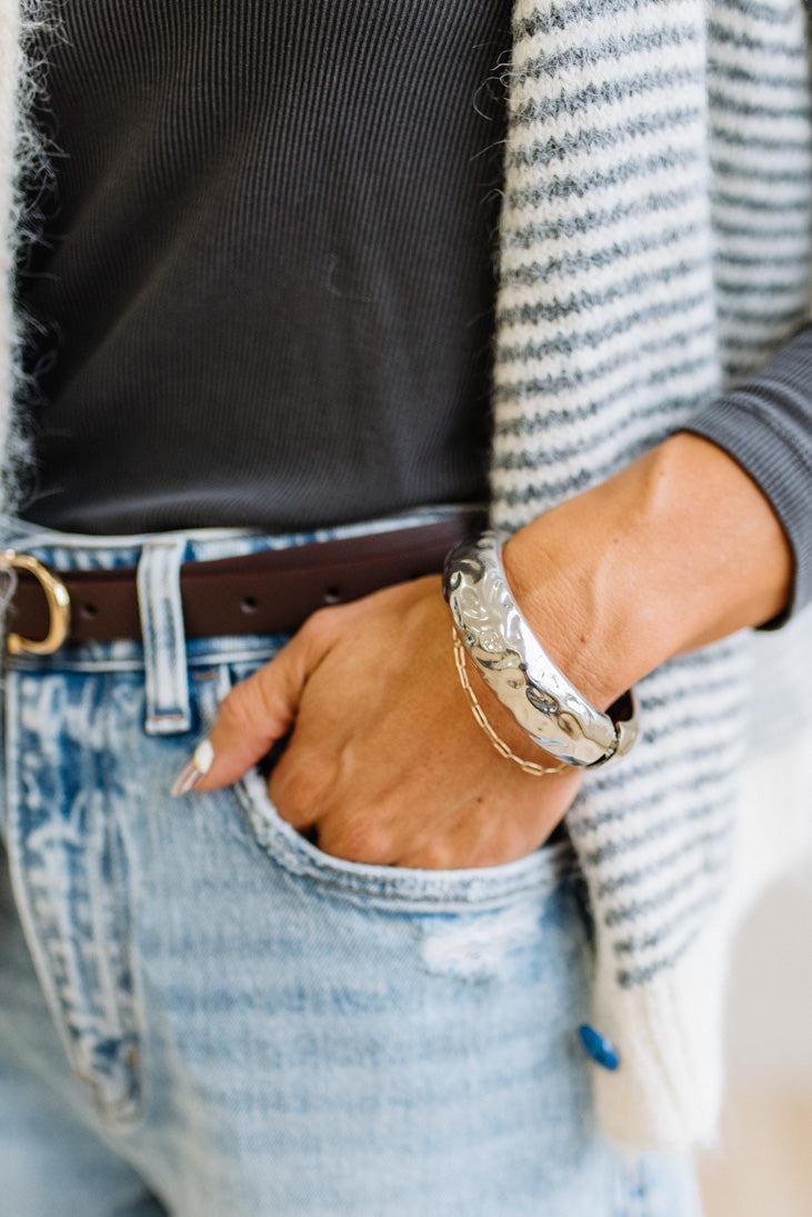 Woman in striped top and light jeans with her hand an a pocket and focused on a large silver bangle.