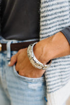 Woman in striped top and light jeans with her hand an a pocket and focused on a large silver bangle.