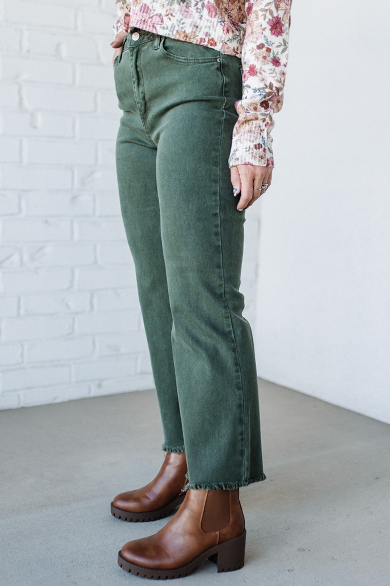 Person wearing green jeans and brown boots against a white brick wall.