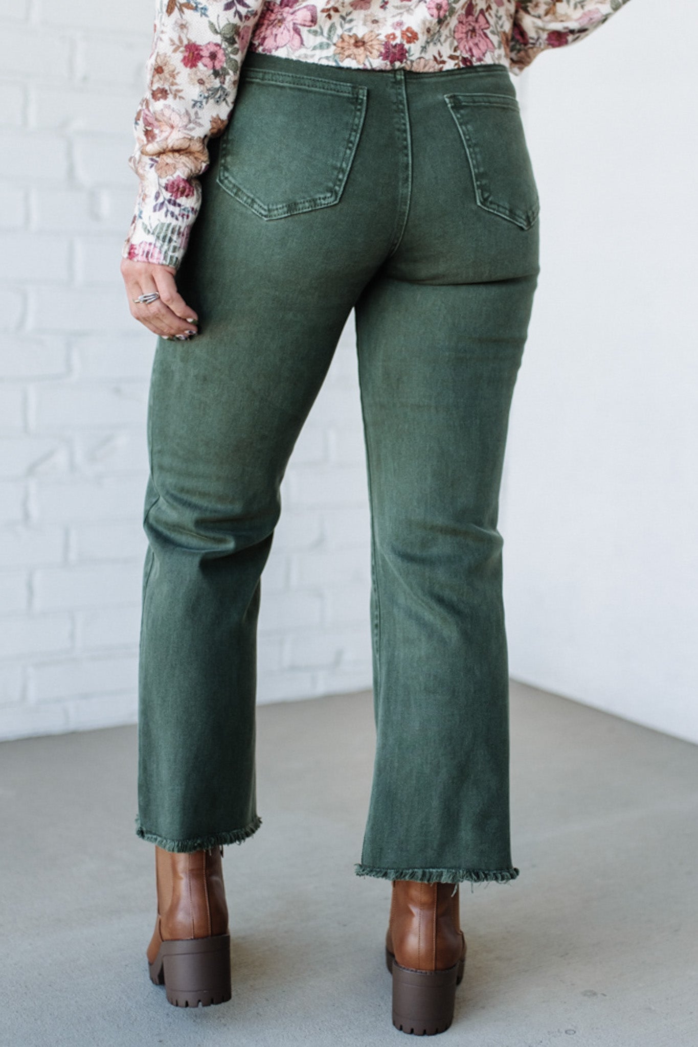 Person wearing green jeans and brown boots against a white brick wall.
