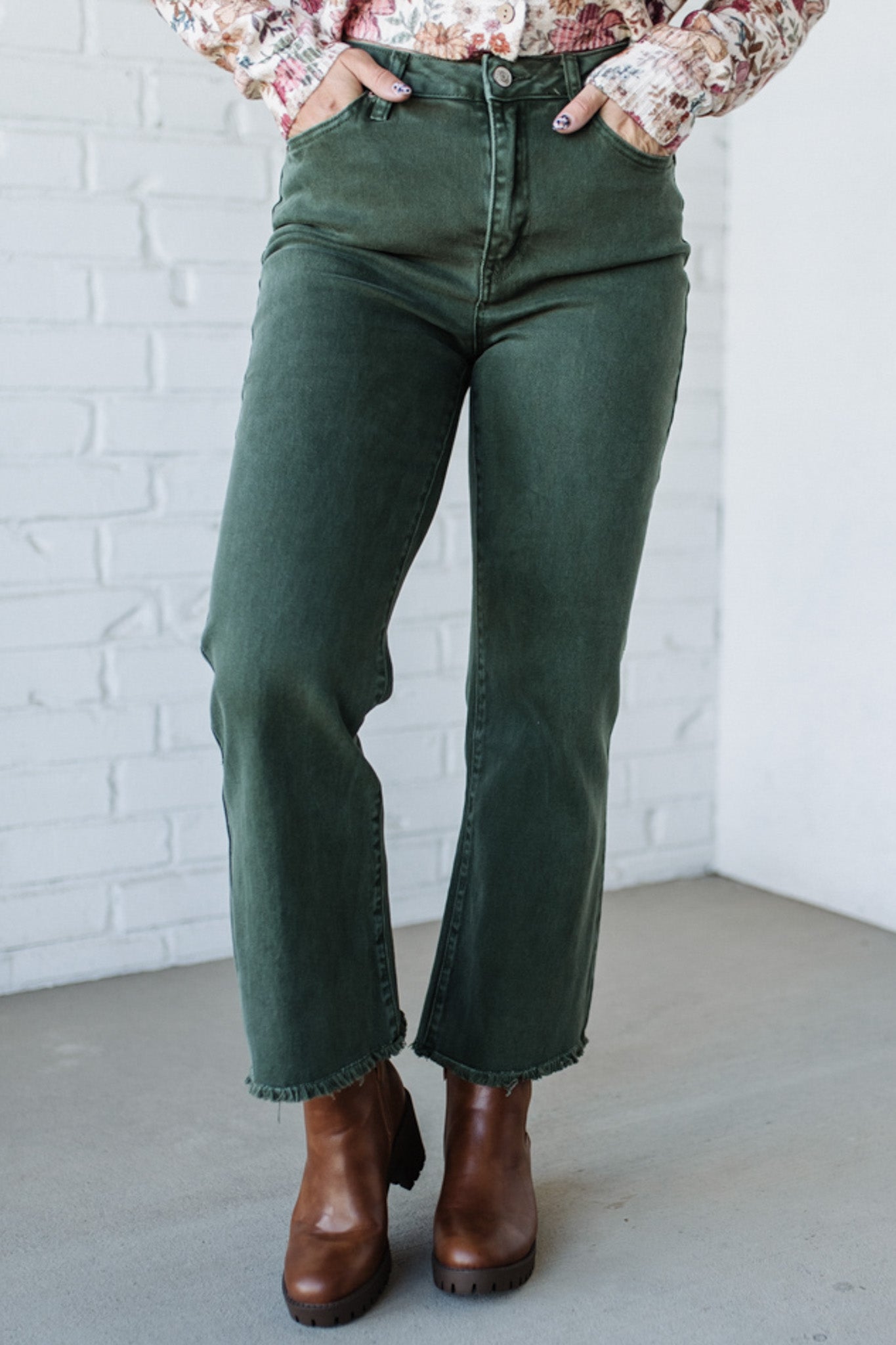 Person wearing green jeans and brown boots against a white brick wall.