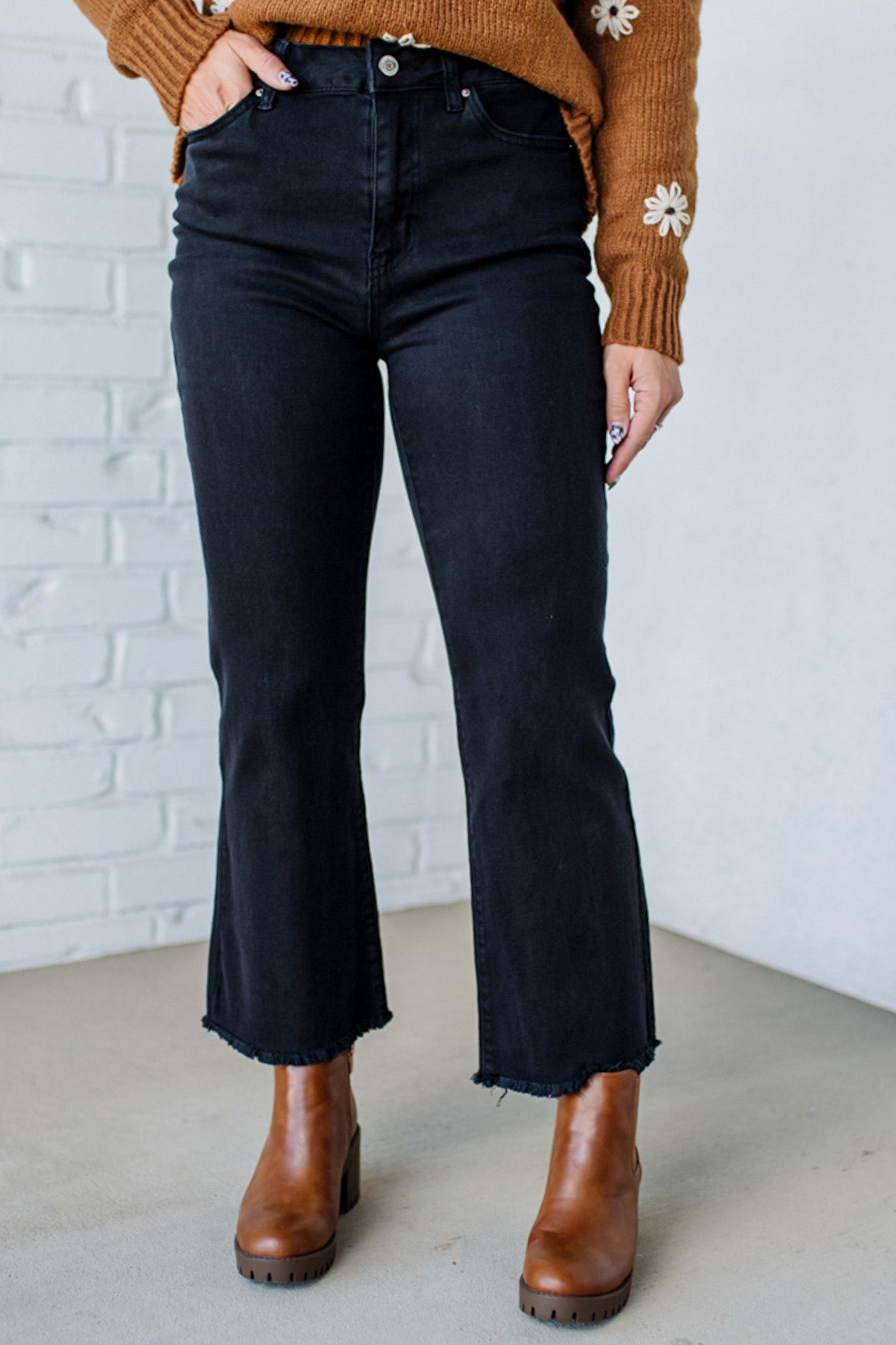 Person wearing black jeans and brown boots against a white brick wall.