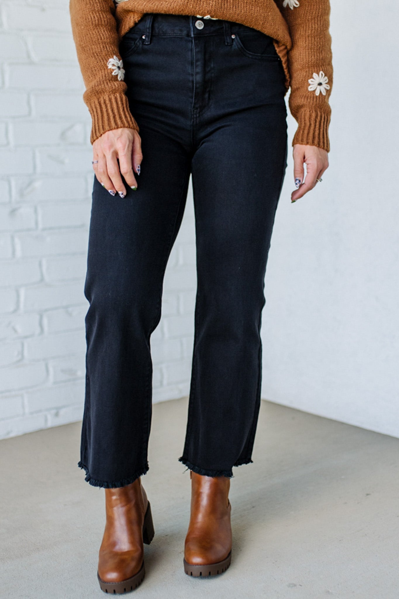 Person wearing black jeans and brown boots against a white brick wall.