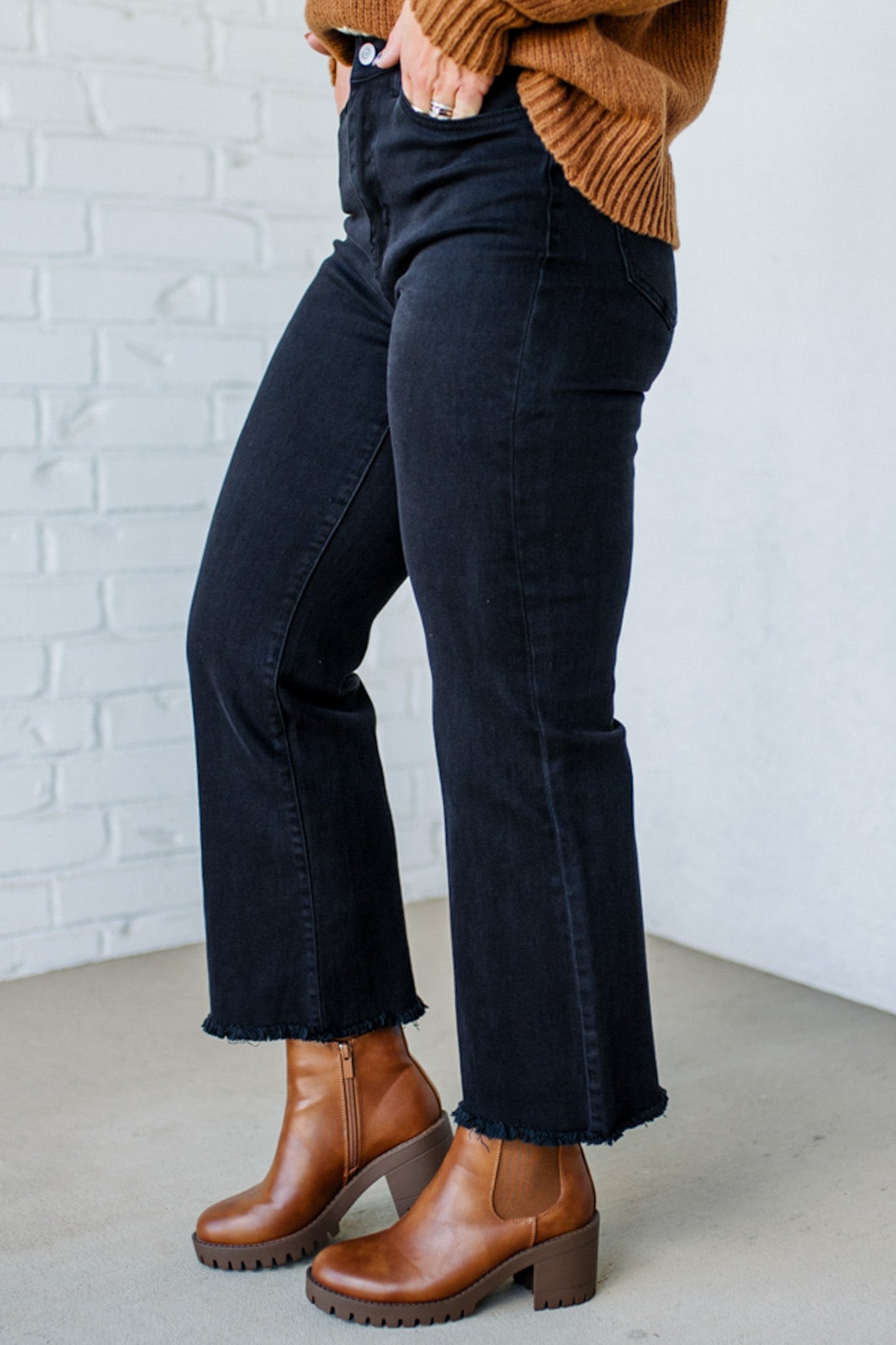 Person wearing black jeans and brown boots against a white brick wall.