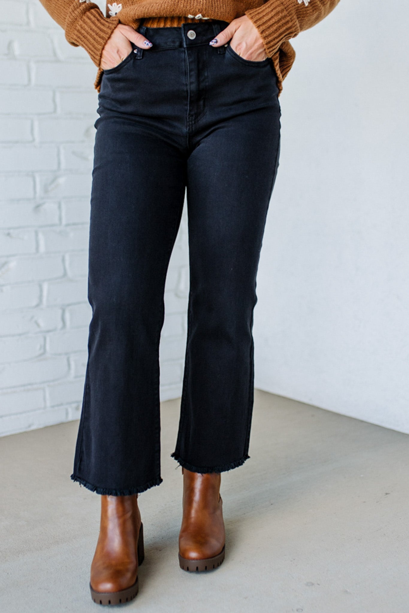 Person wearing black jeans and brown boots against a white brick wall.