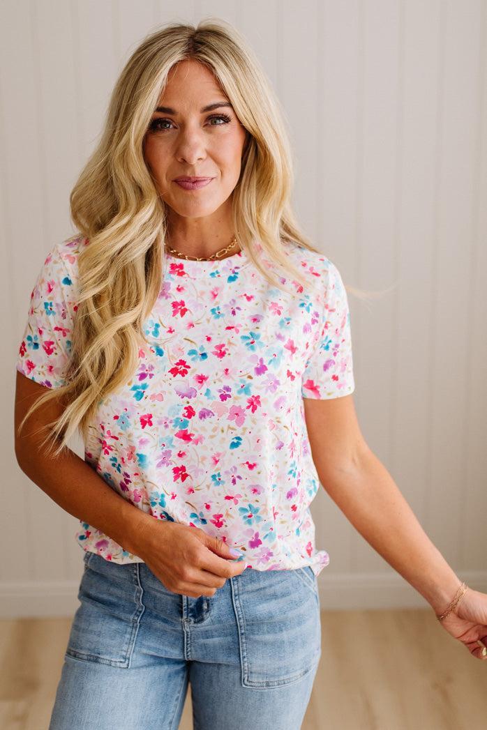 Woman wearing a colorful floral top and blue jeans against a neutral background