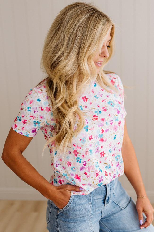 Woman wearing a floral top and jeans against a neutral background