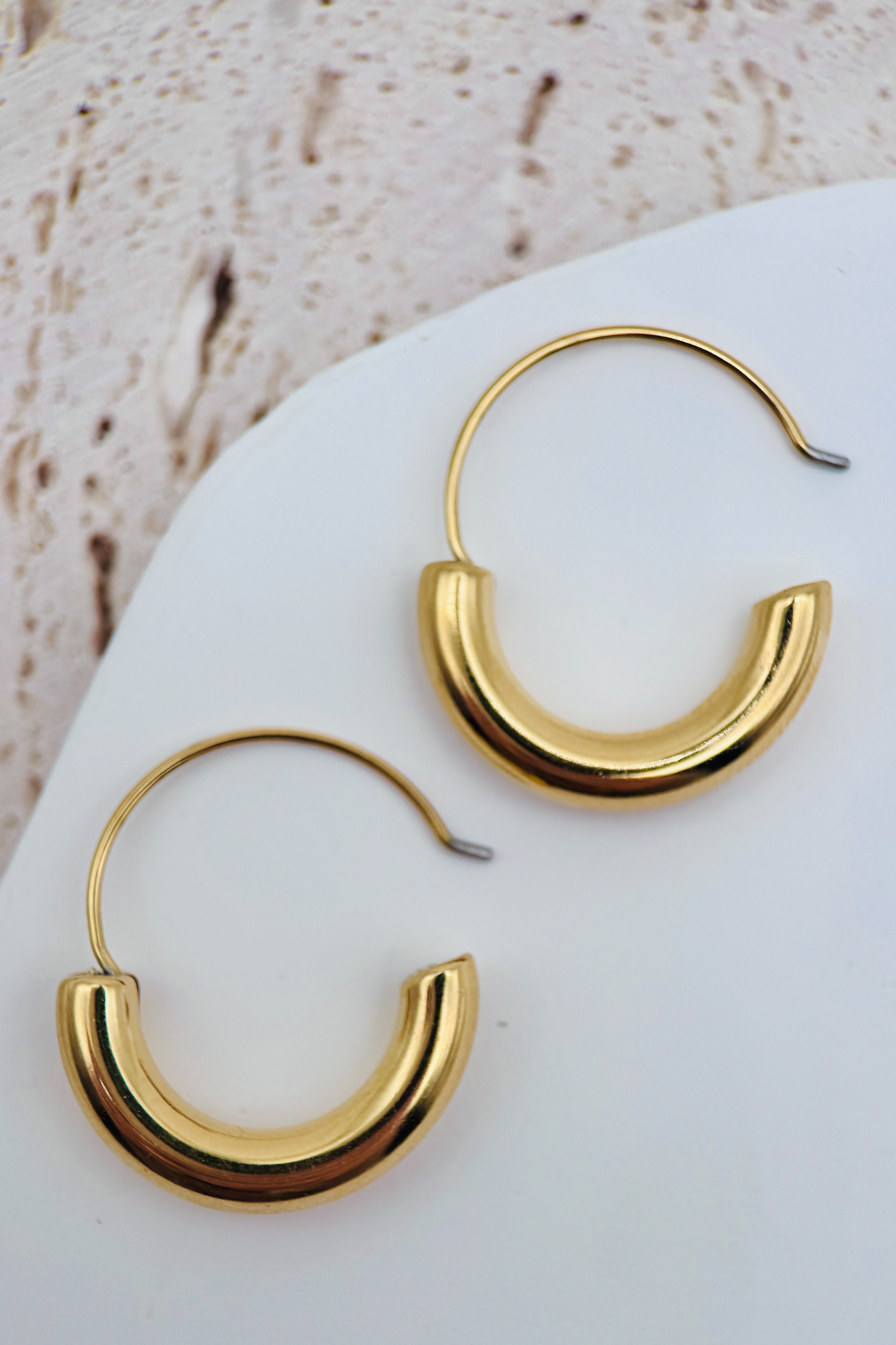 Gold hoop earrings on a white stone surface